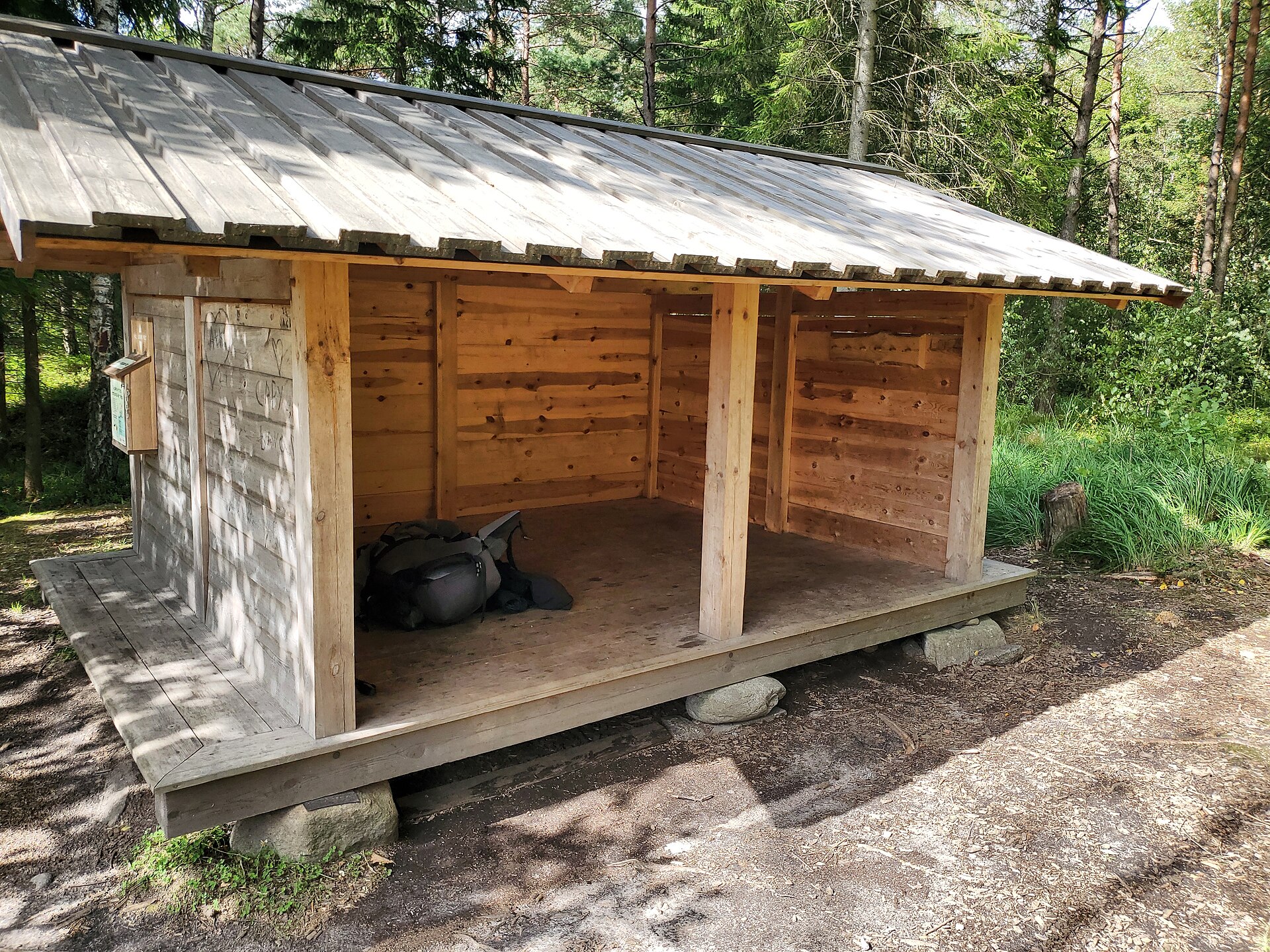 Et træshelter med plads til overnatning omgivet af skov.