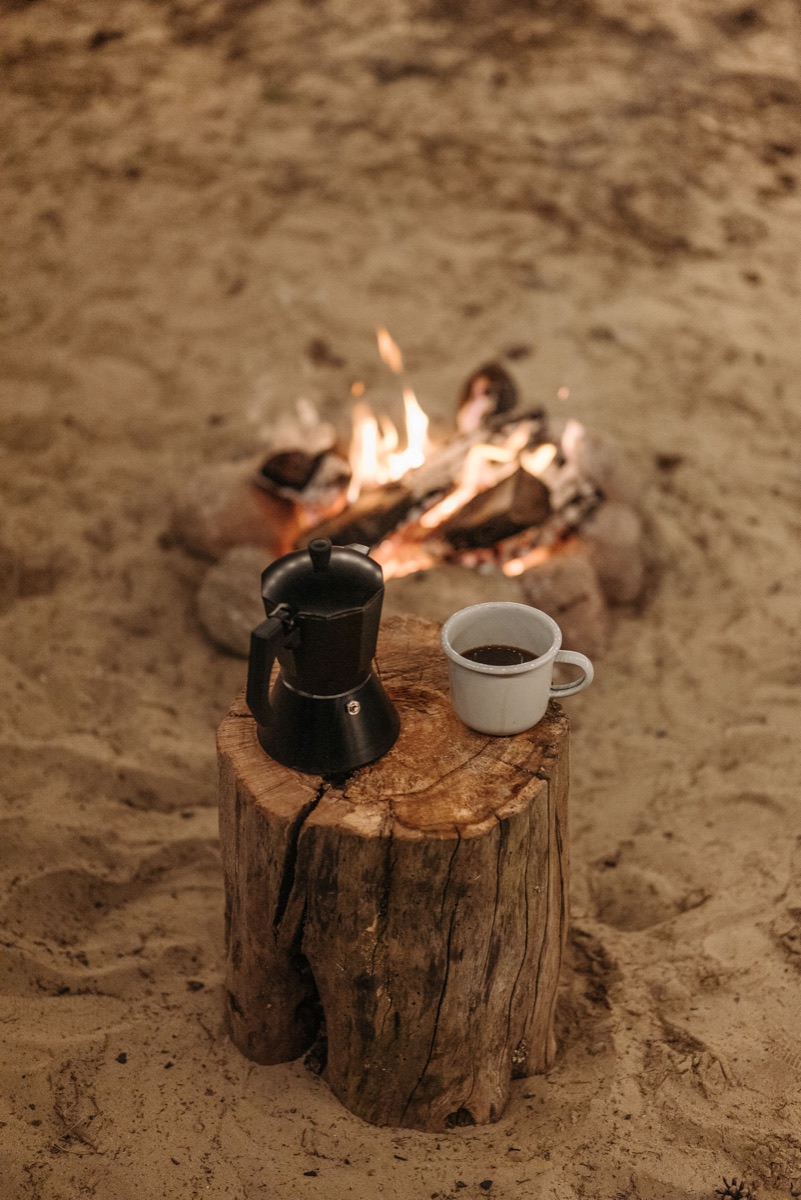 Kaffekande og kop ved et lille bål på en træstub.
