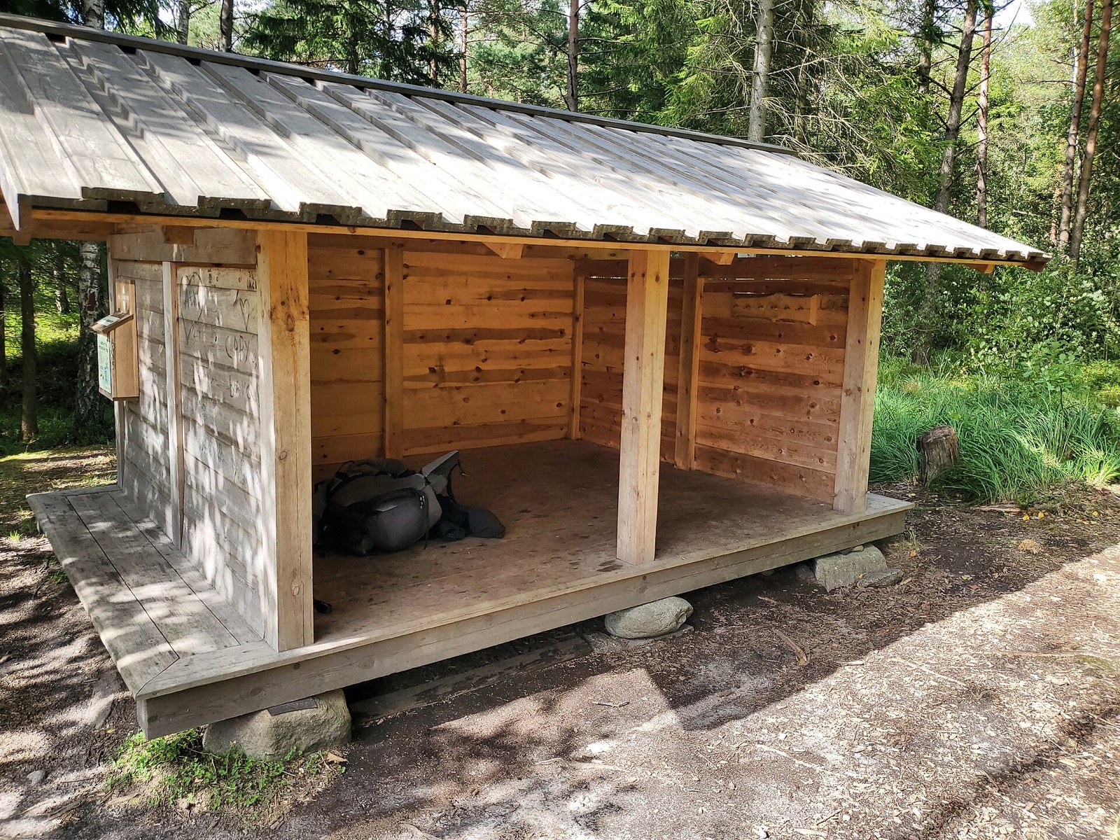 Et åbent træshelter med tag og soveplads i skoven.